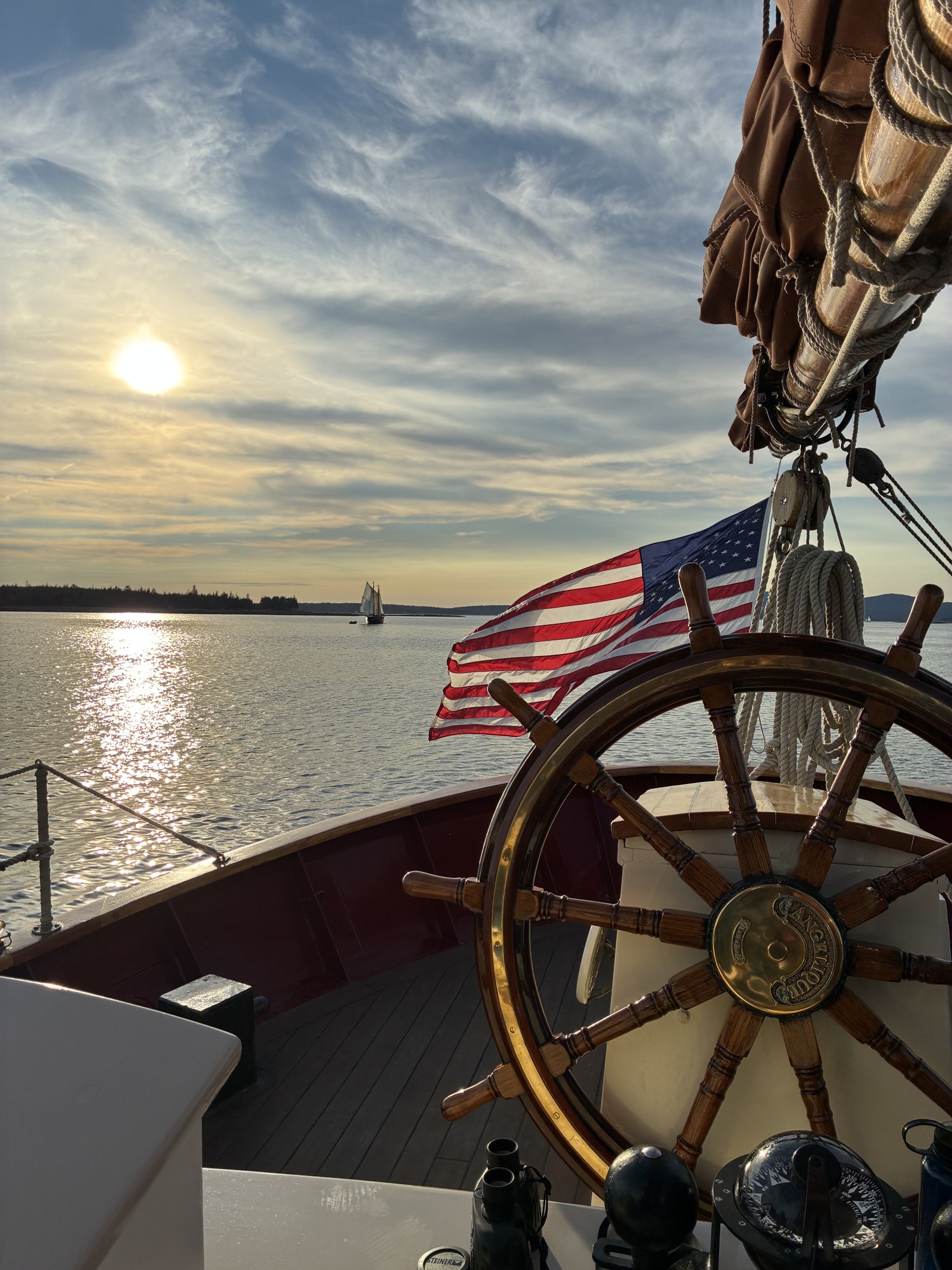 A wooden sailing helm and American flag overlooking sunlit water