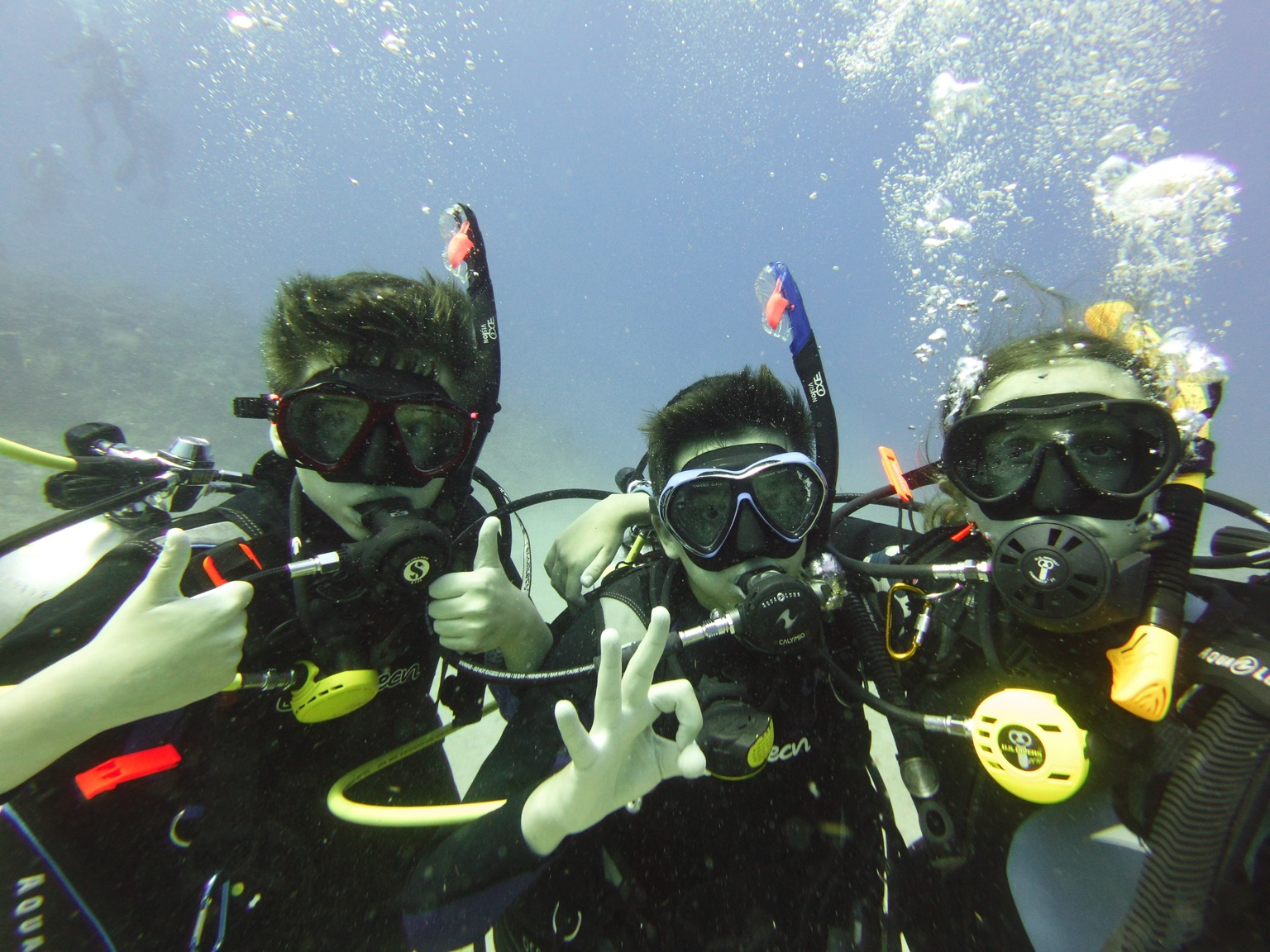 Three scuba divers posing together underwater with thumbs-up and OK hand signals