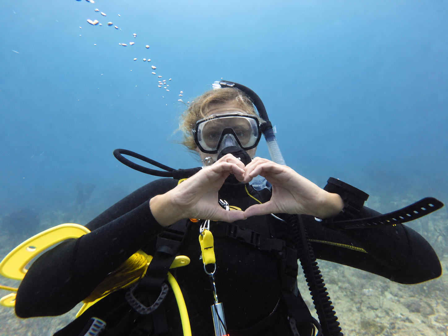 A scuba diver making a heart shape with their hands underwater